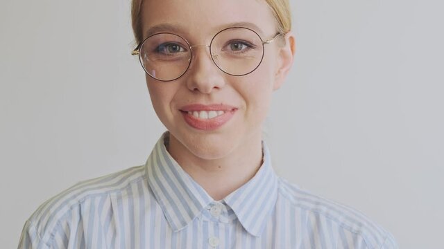 A happy pleased young blonde woman architect wearing glasses is opening her eyes and looking to the camera isolated over white wall in the office