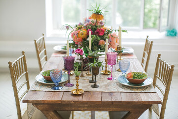 Served table for festive dinner in style boho chic. Decor from fresh flowers peonies, roses, orchids and Leucospermum conocarpodendron surrounded by dishes of plates, glasses and candles. Top view.
