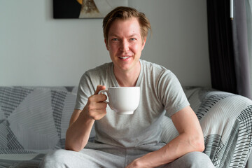 Happy young handsome man drinking coffee in the living room at home