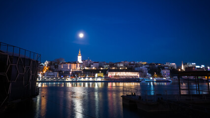 Fototapeta na wymiar Night landscape of Belgrade from the bank of the river Sava, full moon in the sky above the city.