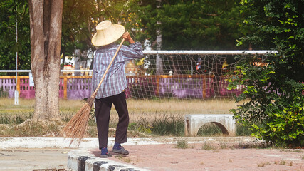 Old female cleaner and holding a sweep at the park.