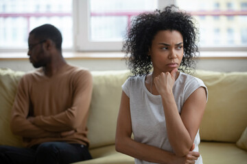 Fototapeta na wymiar African wife looking dissatisfied sitting on sofa with husband apart, couple thinking about problems in relations, feels annoyed and unhappy. Break up relationships end, decision about divorce concept