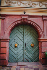 Krakow, Poland - 2012: Red stucco arc with beautifully decorated green wooden door and golden handels.