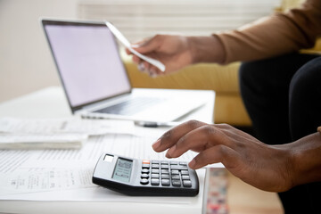Manage planning family budget, savings and payment concept. Close up image hands of African man using calculator calculates finances checking family expenses, do small business, month result analysis