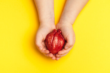 Heart disease prevention, kid hands holds heart on yellow background. Heart attack, high blood...