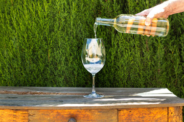 Mano de hombre con una botella de vino blanco sirviendo rn un copa sobre un fondo mesa de madera...