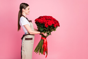 Profile side view portrait of her she nice attractive lovely cheerful girl seller holding in hands giant bunch red roses Valentine day order client service isolated over pink pastel color background