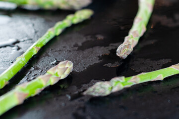 Creatively laid out sprouts of fresh and juicy green asparagus on a black wet background
