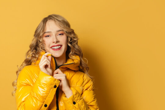 Young Smiling Woman In Winter Jacket On Bright Yellow Background, Close Up Portrait