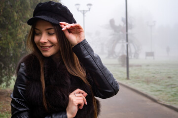 Smiling girl in trench coat walks in park with bouquet of autumn leaves on foggy morning.
