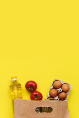 Food delivery, donation. Eggs, pasta, canned food, oil in a string bag on yellow background. Copy space, flat lay. Crisis food stock for coronavirus quarantine isolation period.