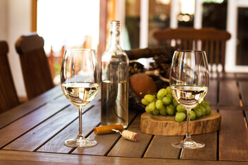 Botella de vino blanco junto a dos copas con vino y uvas sobre una mesa rústica de madera en el...