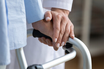 Physiotherapist touches disabled elderly woman hand while she holding walking frame close up view. Nurse supporting patient during exercise rehabilitation therapy. Caregiving, help, eldercare concept