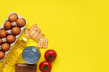 Paper yellow background with food supplies biscuits, buckwheat, eggs, tomatoes, canned goods, butter for the period of quarantine isolation on a yellow background. Copyspace. Flatlay