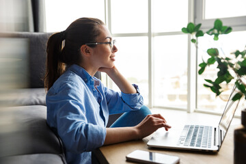 Image of pleased woman working with laptop and smiling while sitting