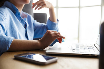 Cropped image of woman working with laptop and cellphone while sitting