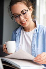 Image of woman reading book and drinking coffee while sitting at table