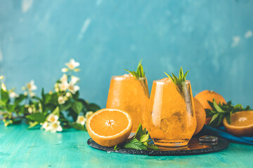 Two glasses of orange ice drink with fresh mint on wooden turquoise table surface. Fresh cocktail drinks with ice fruit and herb decoration. Alcoholic non alcoholic beverage, summer fresh drink