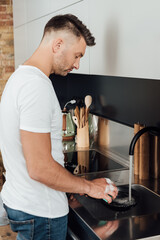 Side view of handsome man cleaning frying pan with sponge in kitchen