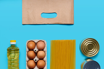 Top view, flatlay. Set of products with paper bag on the blue background. Food from the store. Sunflower oil, eggs, canned food, pasta. Delivery and donation concept