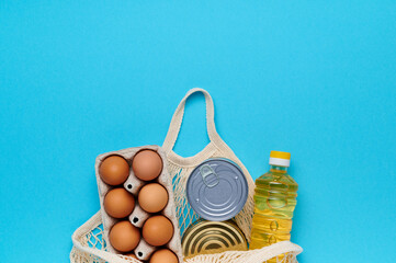 Top view, flatlay. Set of products inside string bag on the blue background. Packaging food from the store. Sunflower oil, eggs, canned food. Delivery and donation concept