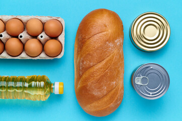 Top view, flatlay, computation. Set of products on the blue background. Packaging food from the store. Sunflower oil, eggs, canned food, loaf of bread. Delivery and donation concept