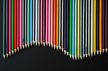 Wave of colored pencils on black background - colorful background