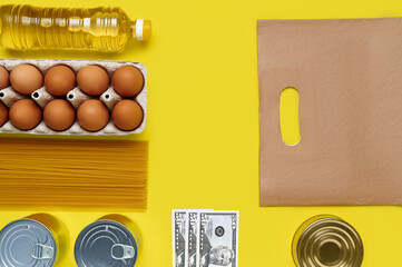 Set of products on yellow background with paper bag and us dollar cash banknotes, flatlay, top view-sunflower oil, chicken eggs, tray, canned, pasta, vermicelli, top view, food, plastic bottle, money