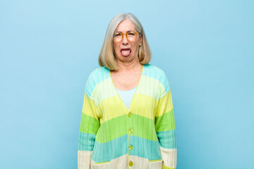 senior or middle age pretty woman feeling disgusted and irritated, sticking tongue out, disliking...