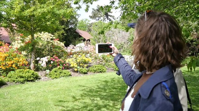 Woman makes Photo with Mobile Smart Phone in City Park with Blooming Flowers