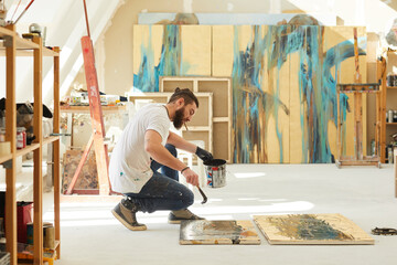 Side view full length portrait of contemporary bearded artist painting abstract picture while...