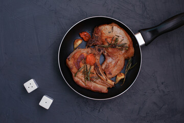 Roasted pork steak in frying pan on black background