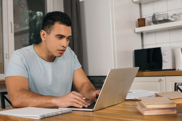 Fototapeta na wymiar handsome mixed race freelancer using laptop near books and notebook