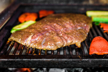 Grilling marinated angus beef flank steak on hot coals barbecue grill.