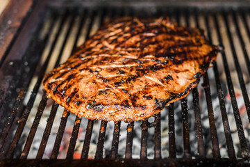Grilling marinated angus beef flank steak on hot coals barbecue grill.