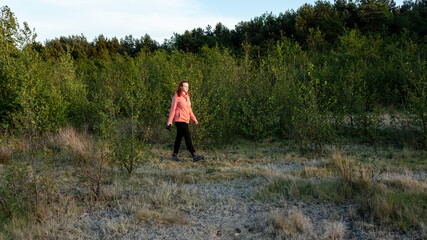 Young woman walking through a meadow carrying a camera, in late evening light.