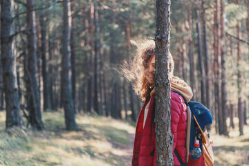 Young pretty woman walks in the forest, smiles and hides behind a pine trunk, local travel trend