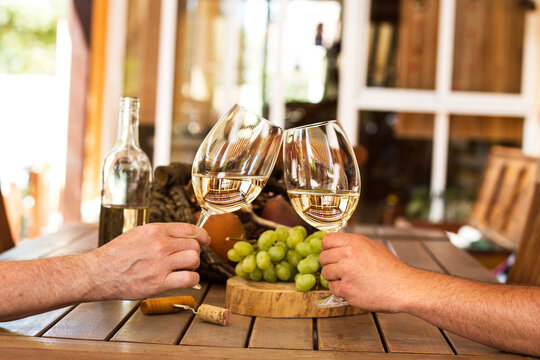 Par de manos brindando con dos copas de vino blanco en una terraza al aire libre. Vista de frente y de cerca