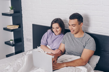 mixed race freelancer using laptop near attractive girl in bed