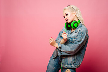 Happy stylish blond woman in pink glasses with big headphones listening music and dancing on colored background