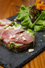 Open prosciutto cheese green salad sandwich on rye bread slices 