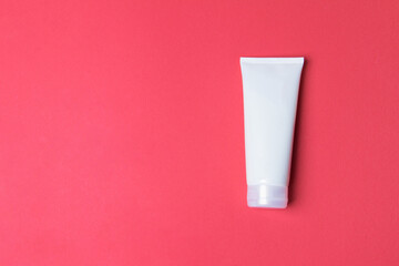 tube with cream on red colored paper background with copy space