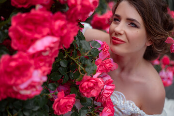 Naklejka premium Portrait of pretty bride dressed wedding white dress, make up and hairstyle posing at the background flowers roses wall at the morning with wind in hair.