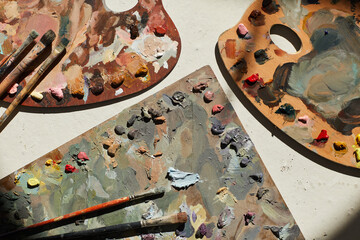 Top down view at artists palettes splattered with paint lying on table lit by sunlight, minimal...