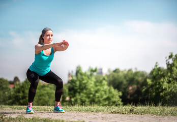 Concentrated and determined young woman doing squats outdoors.