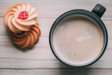 stylish photo of coffee with foam in a black mug top view with sweets and cookies, on a wooden background, natural lighting.