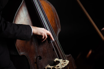 cropped view of musician playing on contrabass on dark stage - obrazy, fototapety, plakaty
