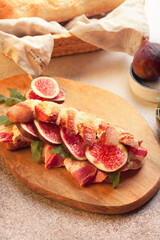 Fresh french baguette with cream cheese, figs, bacon and arugula on a Board with parchment paper