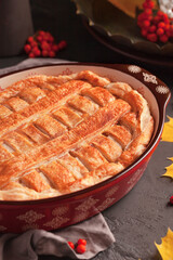 Autumn composition on a dark background. Fresh homemade Apple pie with cinnamon made with puff pastry. The composition includes yellow and orange leaves and mountain ash