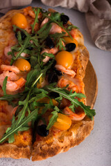 Pizza on thin dough with rucola, yellow tomatoes, cheese and shrimp